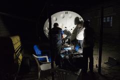 WHO Logistician Kamal Ait-Iklef, IT Specialist Thomas Bikoumou, and Congolese electrician Papy Bekombe work late at night to set up a VSAT link at an outbreak response camp in Itipo in order to facilitate communication from the camp.