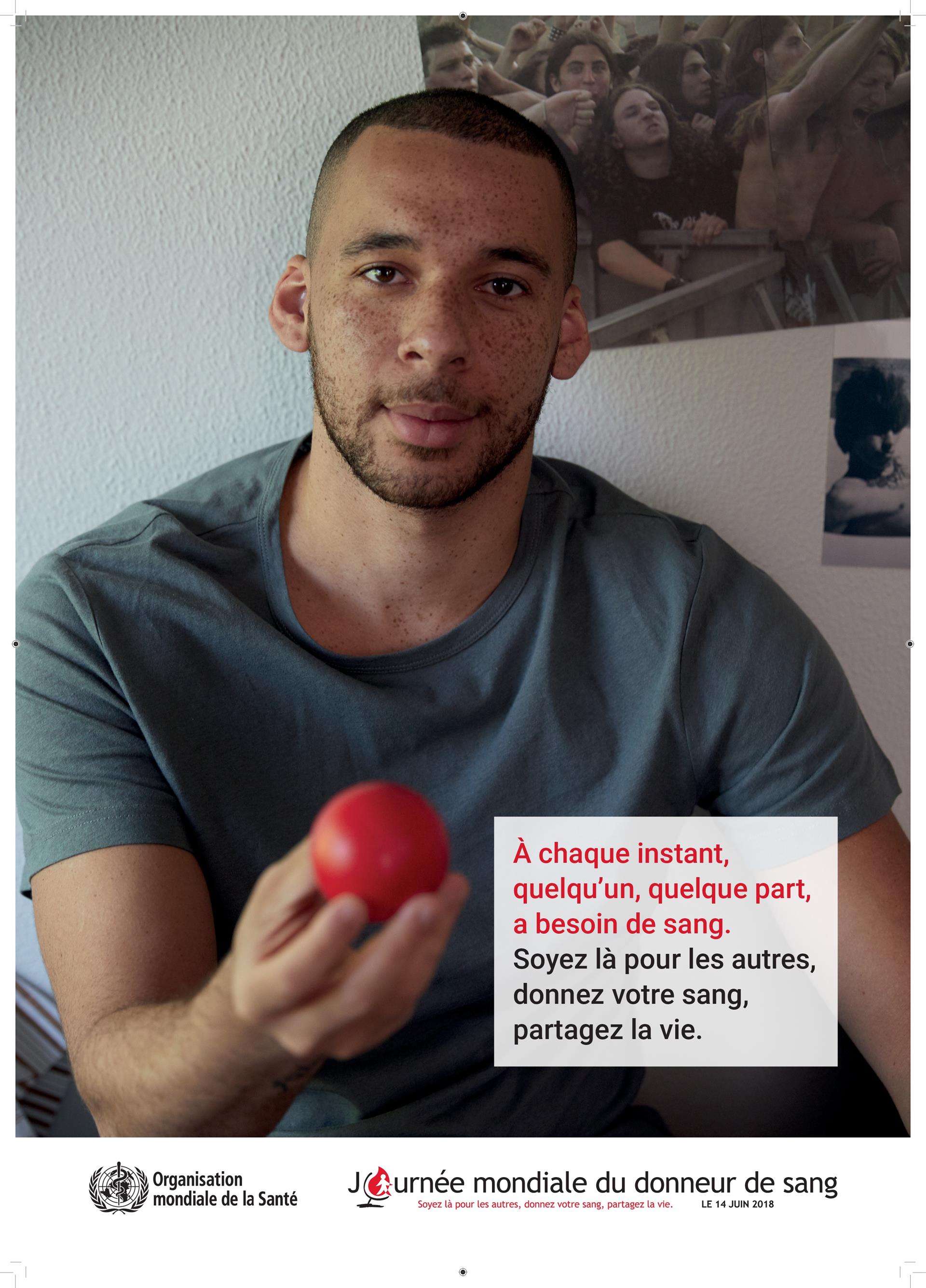 Un jeune homme tend une balle rouge -affiche de la Journée mondiale du donneur de sang 2018 de l'OMS - donnez votre sang partagez la vie