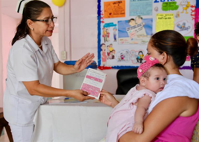 A nurse hands a vaccination card to a mother, holding her young girl, in Nicaragua