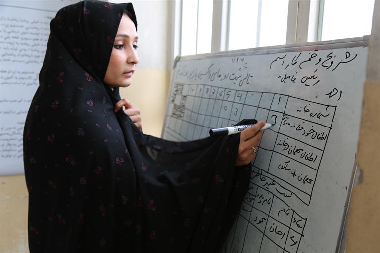 A woman in Afghanistan marking numbers on a whiteboard to track vaccination outreach in the country